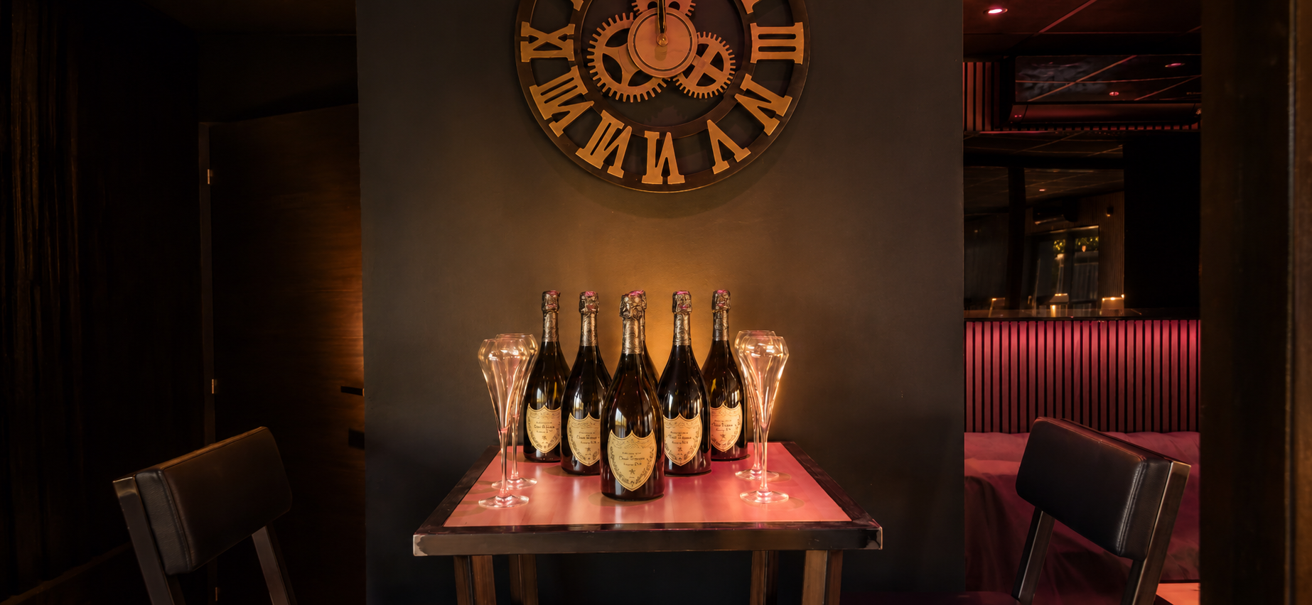 L'horloge de L'Écrin au-dessus d'une sélection de champagnes et de flûtes, dans la lumière feutrée du bar